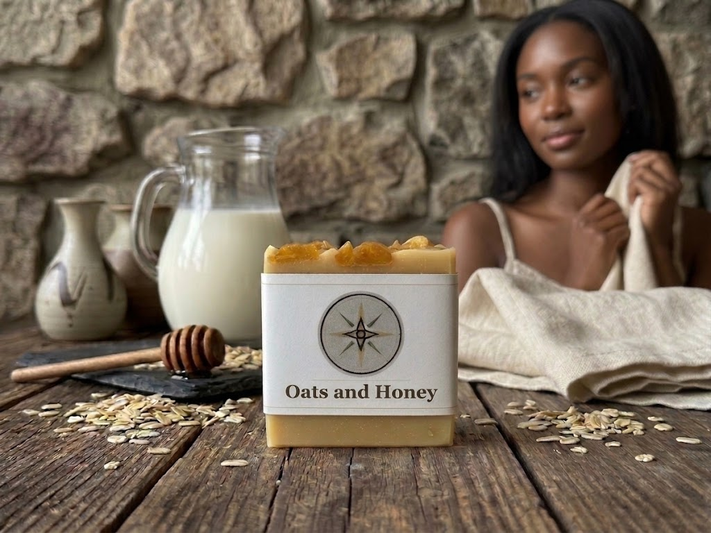 LIFA Oats and Honey goat milk soap bar on a rustic wooden table with a milk pitcher, honey dipper, and scattered oats, with a woman holding a linen towel against a stone wall in the background